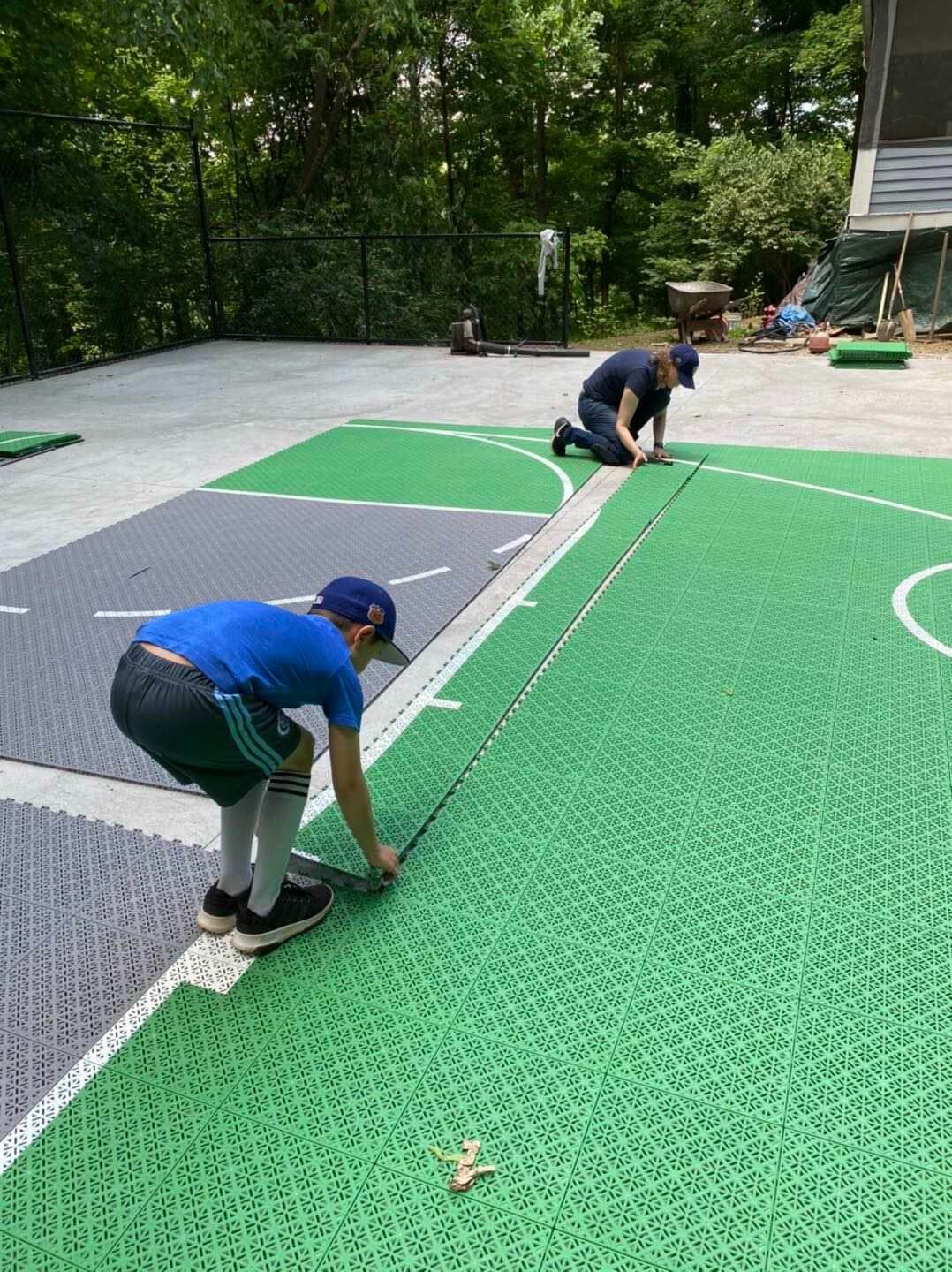 Two people assembling interlocking Swish Tiles on a backyard basketball court.