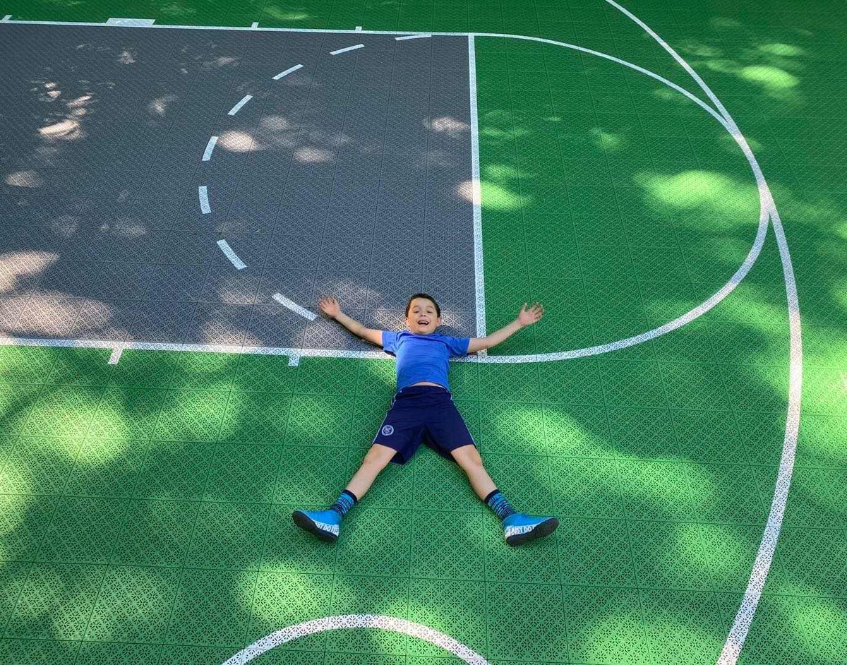 Child lying on a green and gray Swish basketball court.