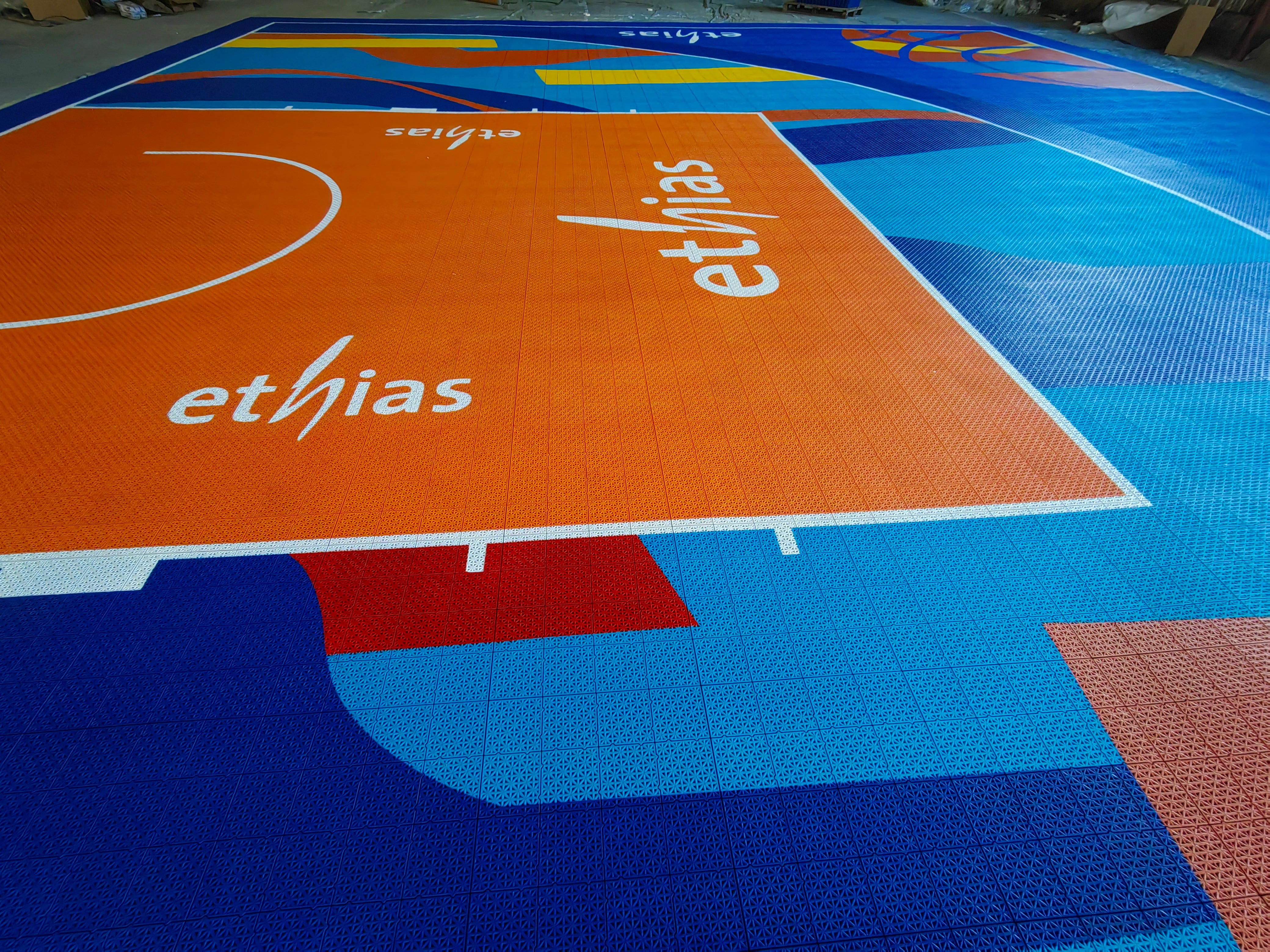 Orange key, blue border, and custom Ethias branding on the modular court tiles